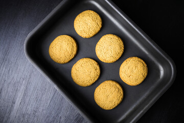 Six round baked biscuits on black oven-tray, view from above