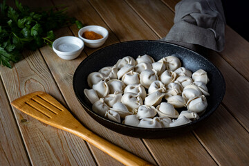 A hearty lunch: dumplings with meat in a large frying pan. Ravioli frozen in a frying pan on a wooden table.