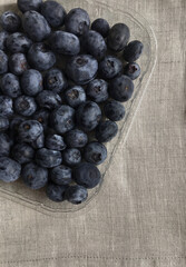 A transparent container with fresh blueberries on a linen tablecloth.