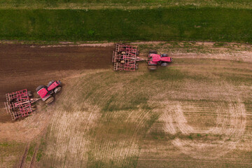 Two tractors with a disc harrow plow the field for sowing. Aerial photography.
