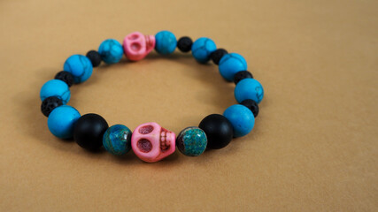 a women's bracelet made of natural stones of turquoise howlite, onyx, black lava and two pink skulls made of howlite lies on a brown background. side view