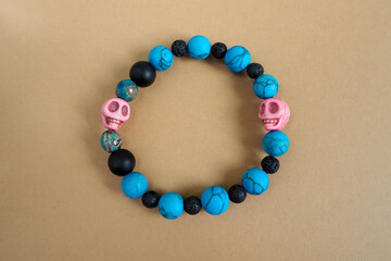 a women's bracelet made of natural stones of turquoise howlite, onyx, black lava and two pink skulls made of howlite lies on a brown background. top view