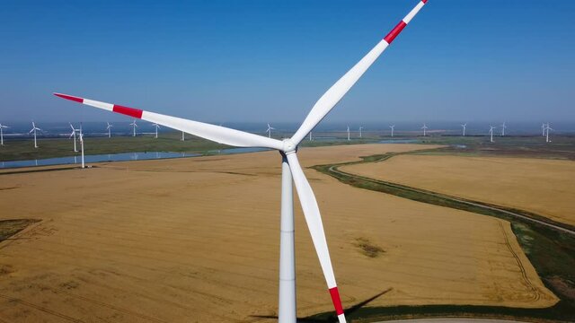 Wind energy working in the field. Large rotating blades. A source of renewable energy. Blue sky. The drone is moving away in a straight line