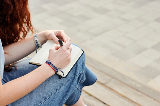 Close-up of a young redhead woman writing in a notebook outdoors
