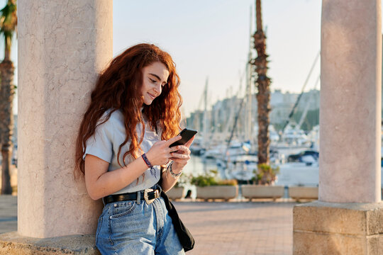 Young redhead woman looks at her mobile in a seaport