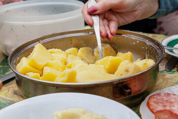 Woman hand lays boiled potatoes from round plate