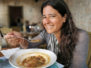 Middle-aged Hispanic woman eating soup and smiling