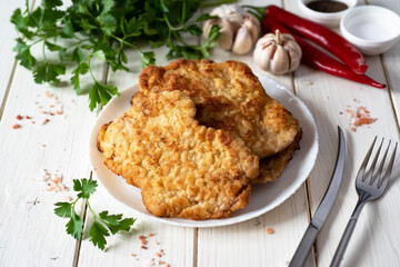 A hearty lunch: pork chops on a white plate , fresh herbs and spices on a white table.