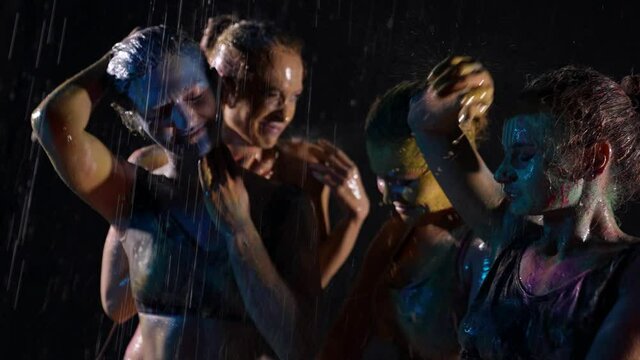art performance four women dancing with paint on the skin in the rain on a black background