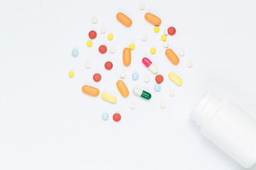 Flat lay composition with bunch of different colorful pills scattered on table from popped plastic bottle. Pile of opened medication on white paper textured background. Close up, copy space for text