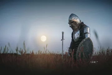 Foto op Plexiglas The tired knight in the plate armor kneels among the battlefield with a sword in the moon light. Lost battle. Defeat concept. © Dmitriy
