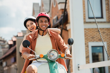 excited interracial couple in hardhats riding scooter on city street