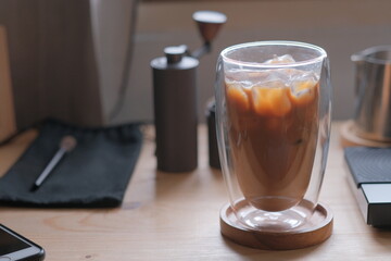 Ice coffee in a tall glass with cream poured over and coffee beans on a old rustic wooden table. Cold summer drink.