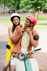 cheerful interracial couple fastening safety helmets before riding scooter