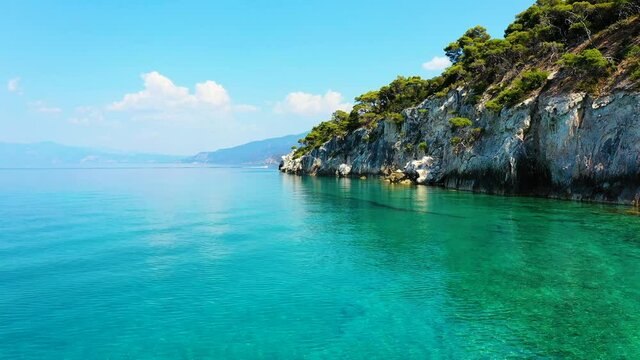 Drone flying low over the sea, near a beach in Mikra Strava in Greece. There is a speedboat sailing fast over the sea, in the background. It is a beautiful sunny summer day.