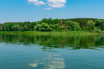 Fototapeta na wymiar Big river Oskol in the east of Ukraine. Beautiful landscape of the river against the background of the forest and the blue sky. White clouds are reflected in the smooth surface of the river.