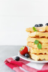 Stack of Belgian waffles, blueberry, strawberry cuts, mint leaf, sugar powder