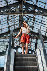 low angle view of stylish asian woman talking on cellphone on escalator