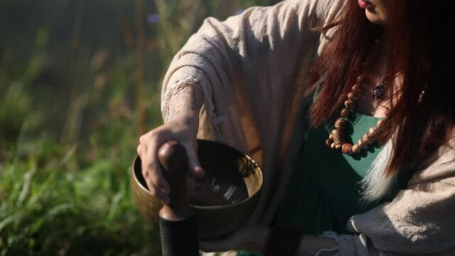 a yogi woman in nature holds a singing massage cup on which the mantra "om mani padme hum" is written 
