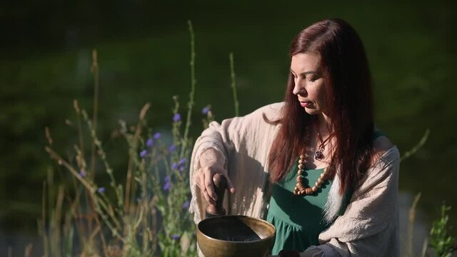 a yogi woman in nature holds a singing massage cup on which the mantra "om mani padme hum" is written 