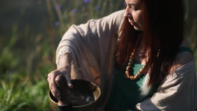 a yogi woman in nature holds a singing massage cup on which the mantra "om mani padme hum" is written 