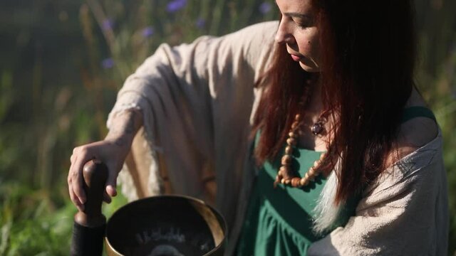 a yogi woman in nature holds a singing massage cup on which the mantra "om mani padme hum" is written 