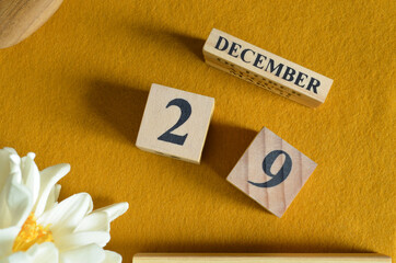 December 29, Wooden Calendar cube on yellow felt fabric with peony flower for date icon background.