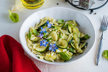 Salad with orzo pasta, fried zucchini and garlic with olive oil dressing in a ceramic bowl on a light concrete background. Orzo salads.