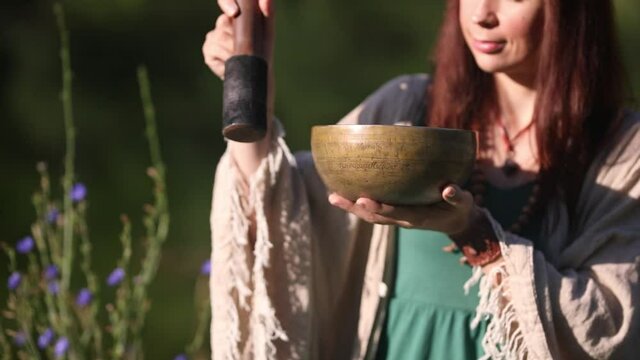 a yogi woman in nature holds a singing massage cup on which the mantra "om mani padme hum" is written 
