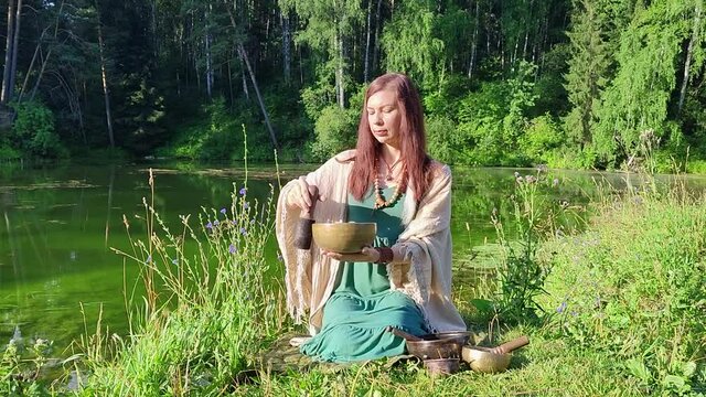 a yogi woman in nature holds a singing massage cup on which the mantra "om mani padme hum" is written 
