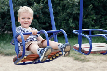 Fototapeta na wymiar Happy, smiling child is swinging on a swings in a park at summer