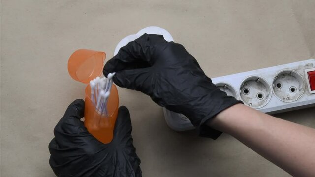 POV hands in black rubber gloves clean dirty plastic extension socket using cotton buds. Cleaning and maintenance of electric extender equipment