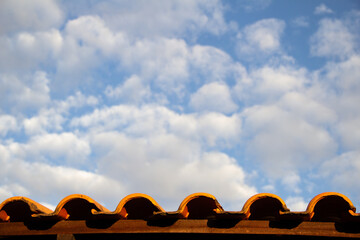 Detalhe do telhado de uma casa com céu azul em um dia claro e cheio de nuvens.