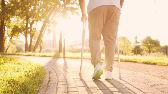 Disabled African-American man is walking with a walker. Handicapped patient in the park. Assistance, rehabilitation and health care. Golden hour sunset.