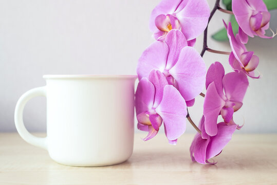 Mock-up of one white mug on table with lilac orchid flowers decor. Template, layout for your design, advertising, logo with copy space. Cup mock up background