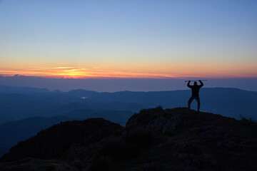 sunset on the mountain, the silhouette of a person on the top of a mountain watches as the sun disappears over the horizon, leaving red and magenta colors