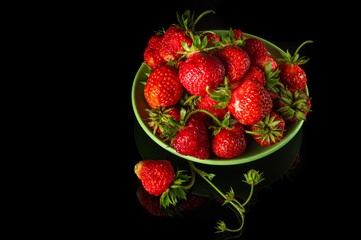A lot of red ripe strawberries in a plate on a black background. Summer diet and vitamin set idea. Free advertising space