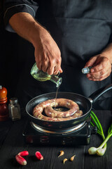 Professional chef adds oil to pan with raw homemade meat sausage. Preparation for cooking sausages in the kitchen of restaurant or cafe on table with vegetables