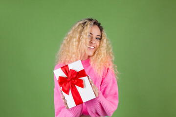 Young blonde woman with long curly hair in pink sweater on green background with gift box happy cheerful excited smiling