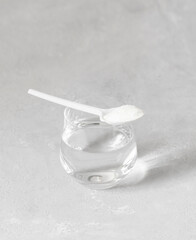 Collagen in a spoon and water on a gray background closeup. Hydrolyzed Collagen protein powder. Natural healthy supplement. Vertical orientation. Space for text.