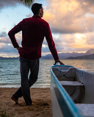 Man standing by canoe in Hawaii on a beach at sunset
