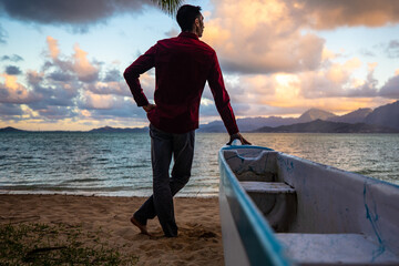 Man standing by canoe in Hawaii on a beach at sunset