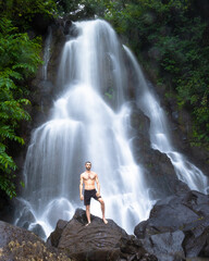 Man standing on a rock in front of a waterfall in paradise
