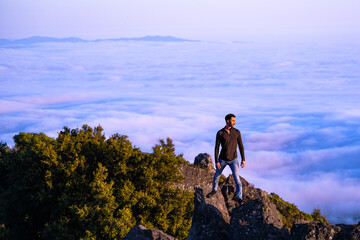 Man standing on a rock above the clouds at sunset