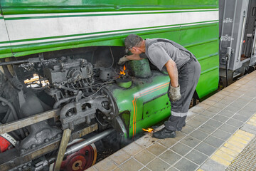 Worker extinguishes an ignited green retro steam locomotive on the railway platform of the Pavshino...