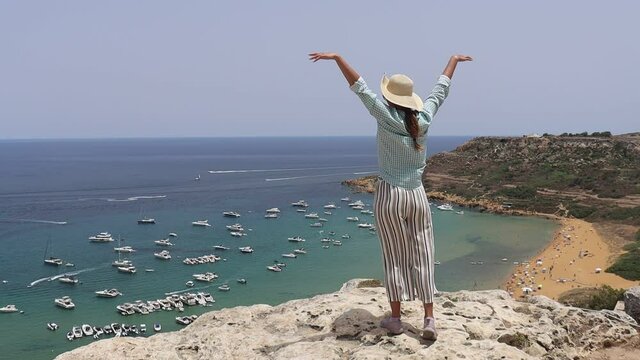 a girl slowly raises her hands at the edge of an abyss in a strong wind on the island of Gozo in slow motion