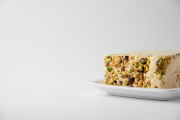Organic halva with pistachios on a white plate isolated on white. Traditional middle eastern sweets. Jewish, turkish, arabic oriental national dessert. Turkish delight concept. Natural vegan product.