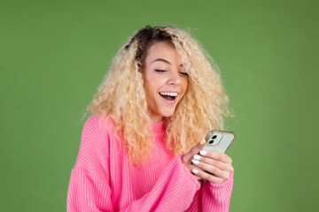Woman in pink sweater on green background holding mobile phone happy smiling cheerful excited