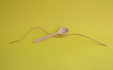 A dry curved stalk of wild onion and a small wooden spoon on a yellow background. The concept of a minimalist decor
