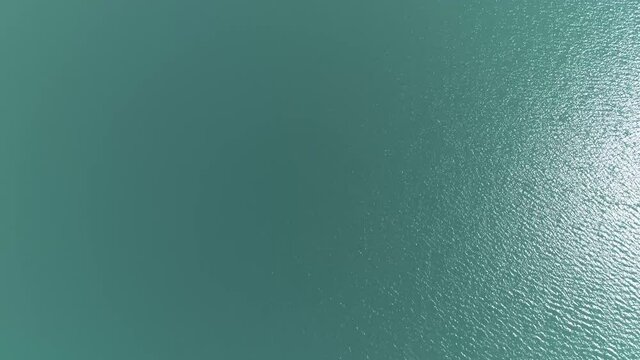 High altitude aerial drone view panning up from the azure blueish fresh lake water to the Alps glacier in the far background also showing a summer blue sky on horizon 4k quality resolution footage